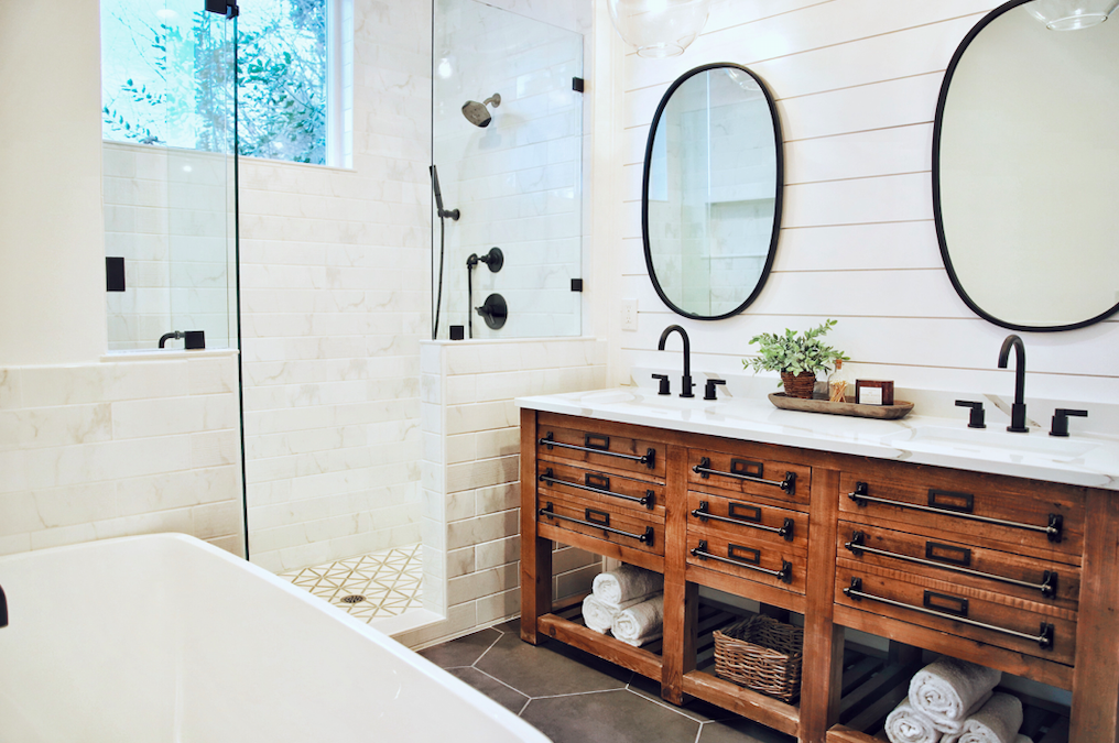 white tiled bathroom with mahogany dresser under his and hers sinks with identical mirrors above them