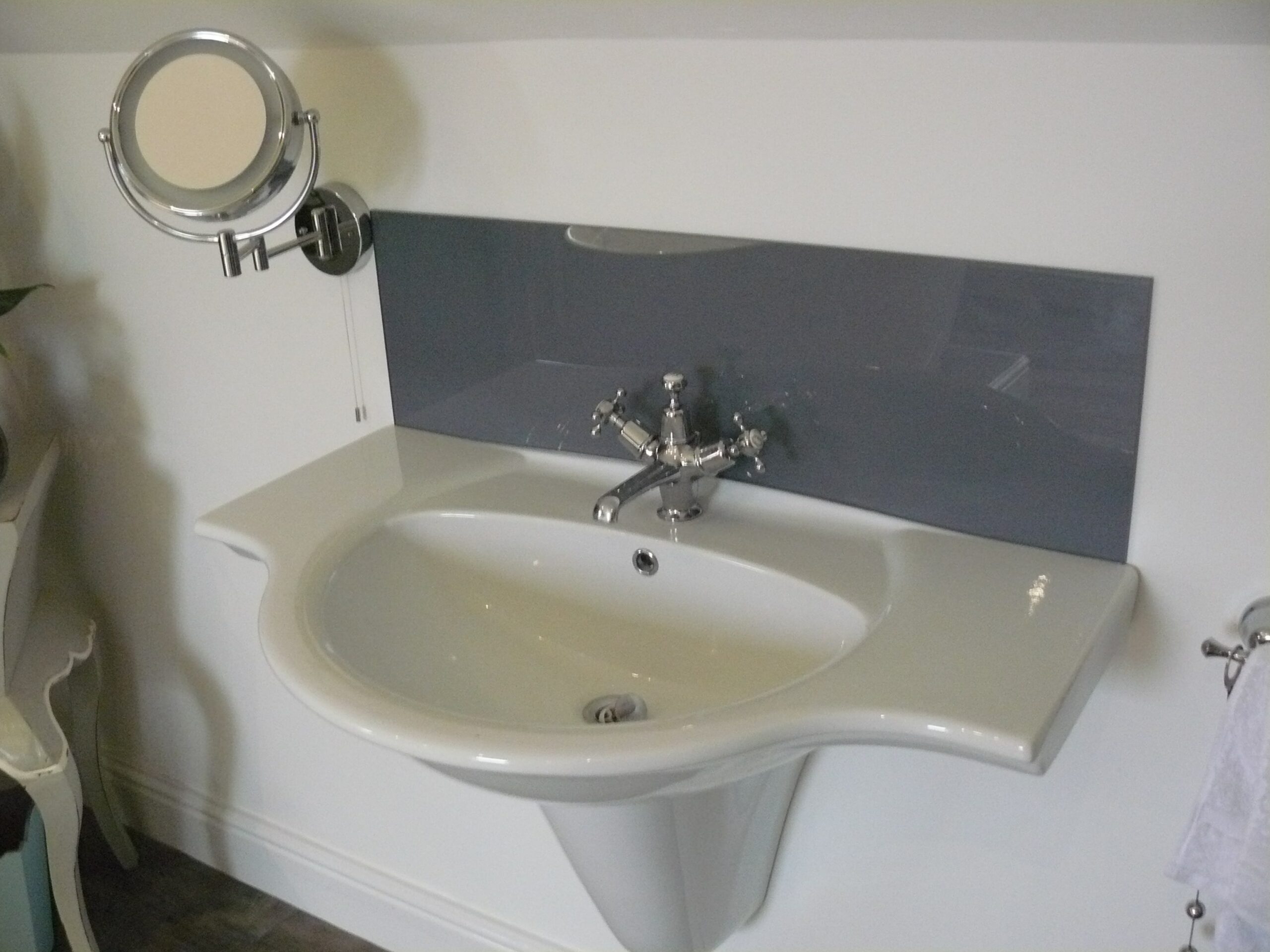 white fixed bathroom sink with silver hardware and grey glass splashback