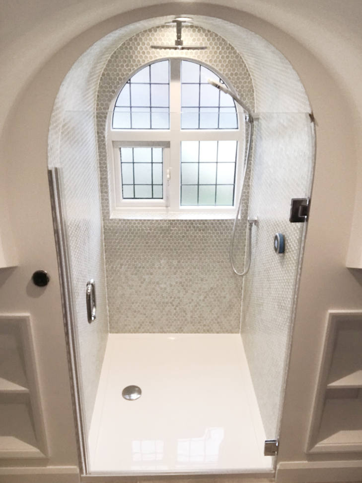 arched stone and concrete walk in shower with frameless glass door