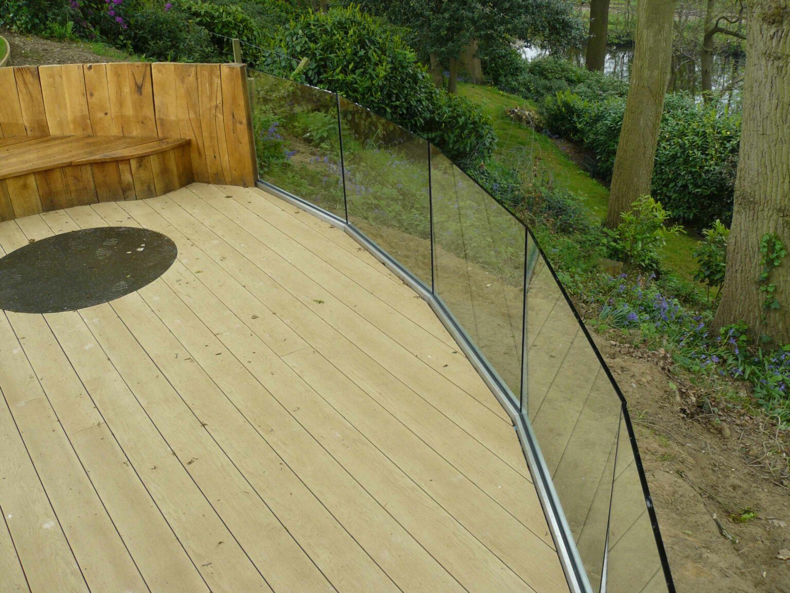 curved glass balustrade surrounding wooden decking area in garden