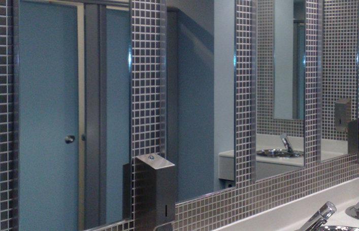 four mirrors fixed to wall of commercial bathroom with squared tiling